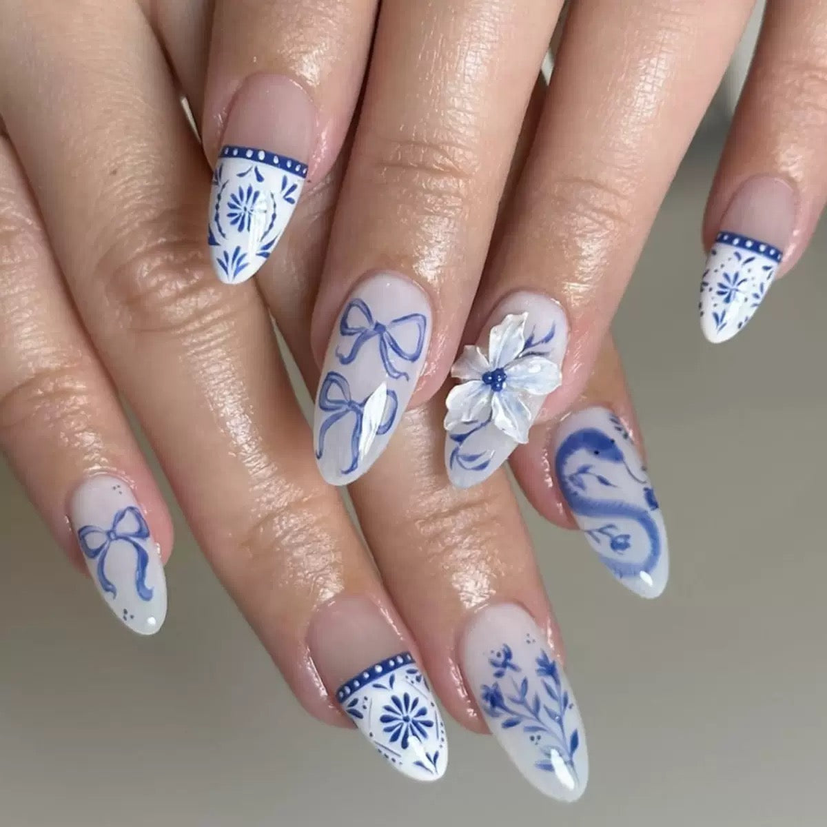 BestSale Chinese-Style Blue and White Porcelain Almond Press-On Nails with Butterfly and Flower Designs on a model's hand.